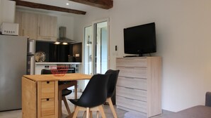 Una cocina compacta con electrodomésticos modernos, un comedor con mesa y sillas de madera y un televisor sobre un mueble.