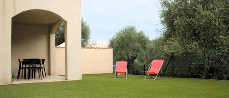 Un patio con mesa y sillas, un espacio de estar cubierto y un césped bien cuidado.