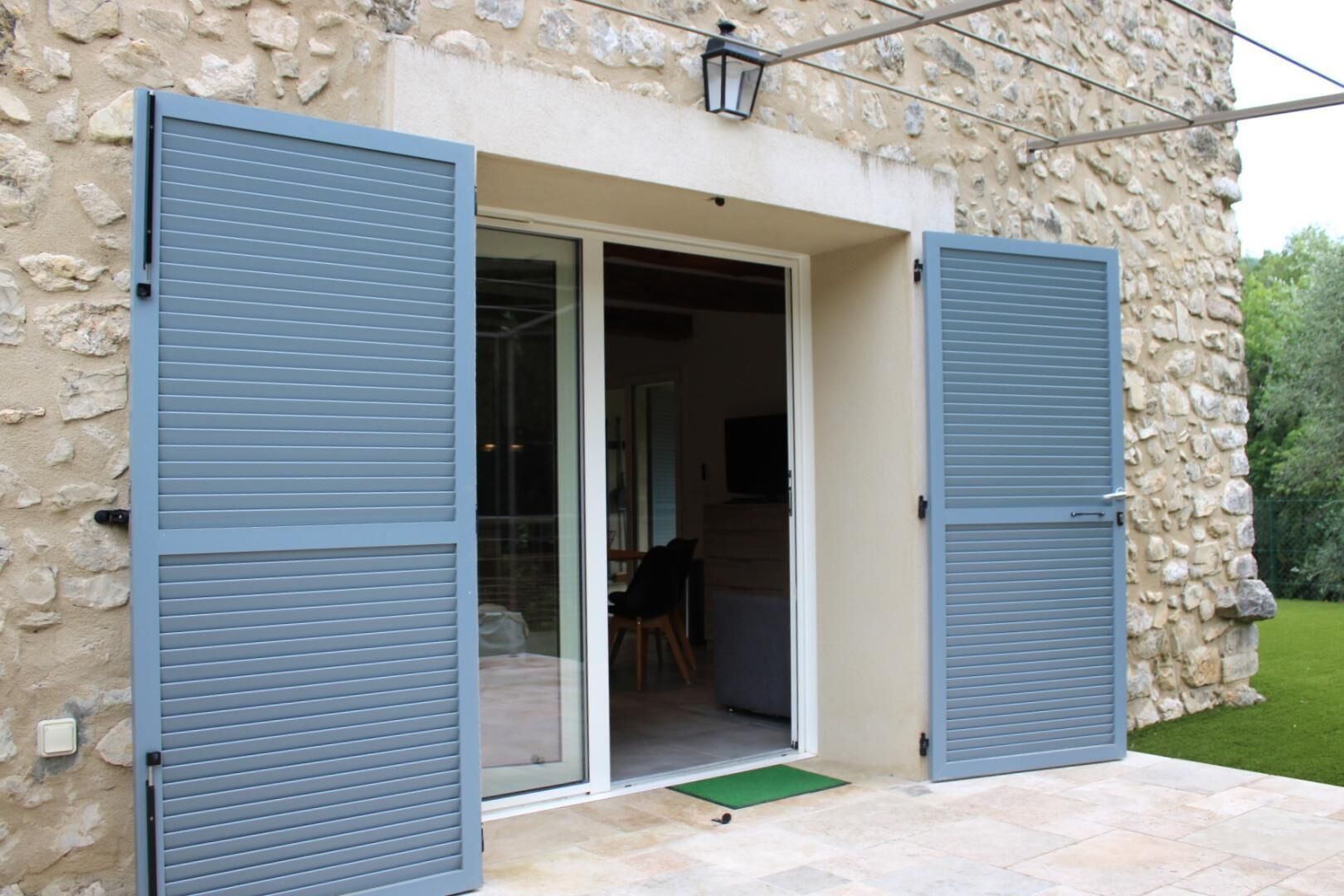 A stone building with a sliding glass door and two blue shutters.