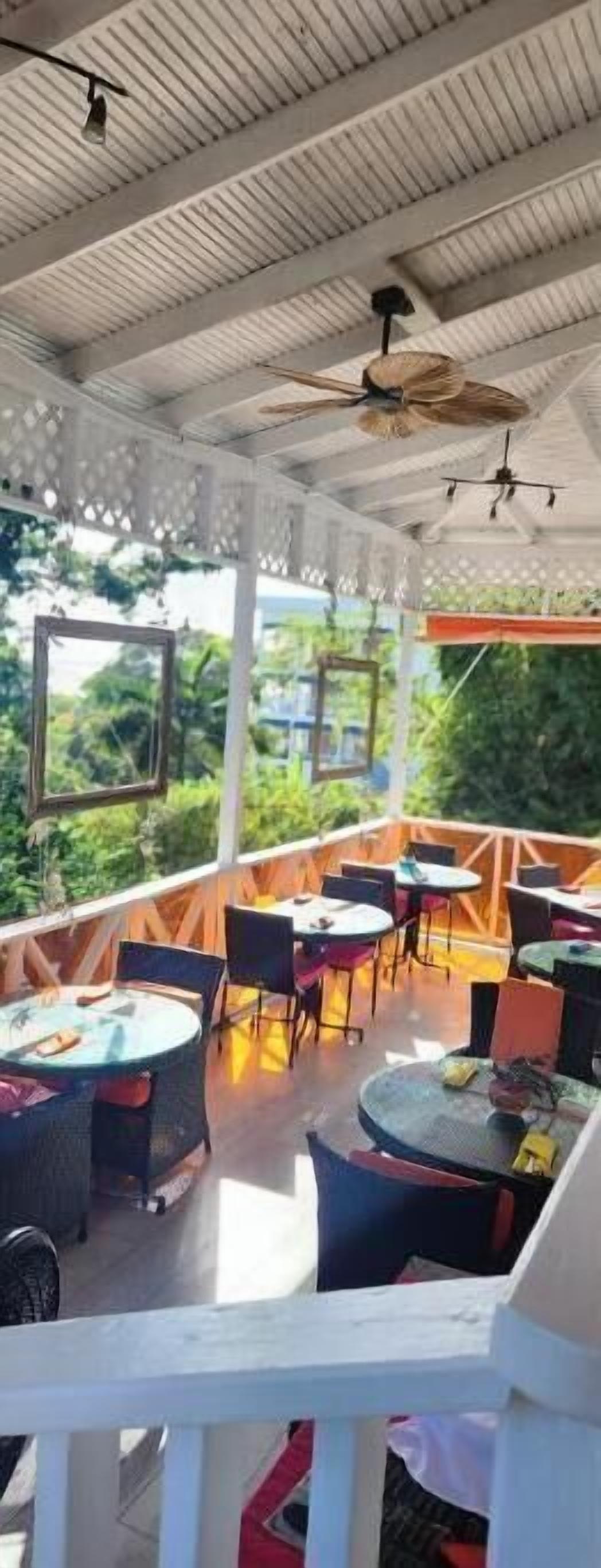 An outdoor seating area with round tables and chairs, a ceiling fan, and a view of greenery.