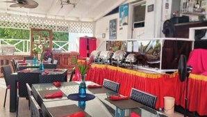 Un restaurante con terraza, mesas con servilletas rojas y un ventilador de techo.