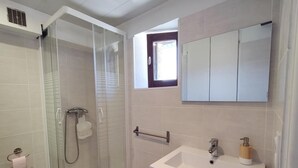 A bathroom with a glass-enclosed shower, a white sink with a wooden soap dispenser, and a mirror above the sink. - Ilonse's Planet 2 (ILONSE)