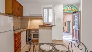 A compact kitchen with wooden cabinets, a built-in oven, and a dining area with a table set for two. - Le Du Guet - Augustus Tower (La Turbie)