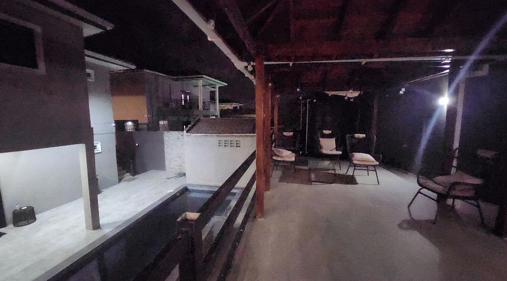 Un espacio interior amplio con una barra larga, una zona de estar pequeña con sillas y una escalera visible que conduce a un nivel superior.