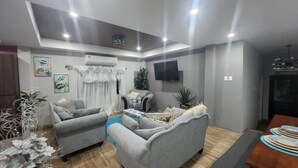Un salón moderno con sofás grises, una mesa de centro y un televisor de pantalla plana montado en la pared.