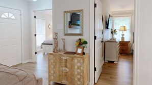A hallway with a wooden cabinet, a mirror, and a door leading to another room.