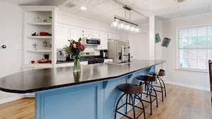 A modern kitchen with a central island, bar stools, white cabinetry, and a decorative vase.