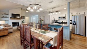 A spacious living room with a fireplace, a dining area with wooden chairs, and a kitchen with stainless steel appliances.