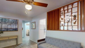 Ein Wohnzimmer mit grauem Sofa, Holzwandverkleidung, Deckenventilator und einem Bild an der Wand.