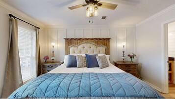 A bedroom with a large bed, a ceiling fan, bedside tables, and a nightstand with a lamp.