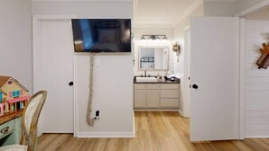 A hallway with a television mounted on a door, a small toy house, and a mirror above a sink.
