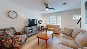 Una sala de estar con televisor, sofá, mesa de centro y sillón estampado.