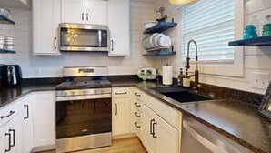 A modern kitchen with white cabinetry, stainless steel appliances, a granite countertop, and a window with blinds.