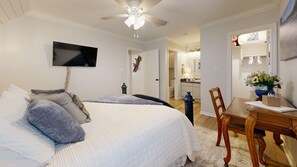 A bedroom with a bed, a TV mounted on the wall, a ceiling fan, and a dining area with a table and chairs. - Central Cottage Charm - Pet Friendly! Very Clean! (College Station)
