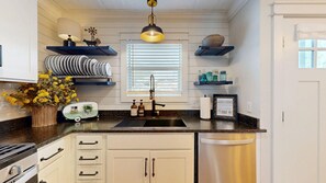 A kitchen with a stainless steel sink, white cabinets, a black countertop, and a hanging light fixture. - Central Cottage Charm - Pet Friendly! Very Clean! (College Station)