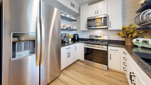 A modern kitchen with stainless steel appliances, white cabinets, and a wooden floor. - Central Cottage Charm - Pet Friendly! Very Clean! (College Station)