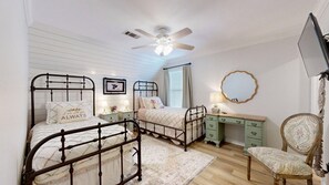 A bedroom with two beds, a desk, a chair, a ceiling fan, and a television.