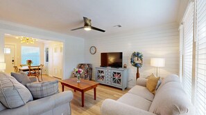 A living room with a sofa, coffee table, TV stand, and a ceiling fan.