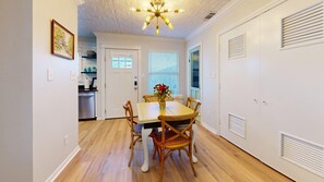 A dining area with a wooden table and chairs, a chandelier, and a kitchen in the background. - Central Cottage Charm - Pet Friendly! Very Clean! (College Station)