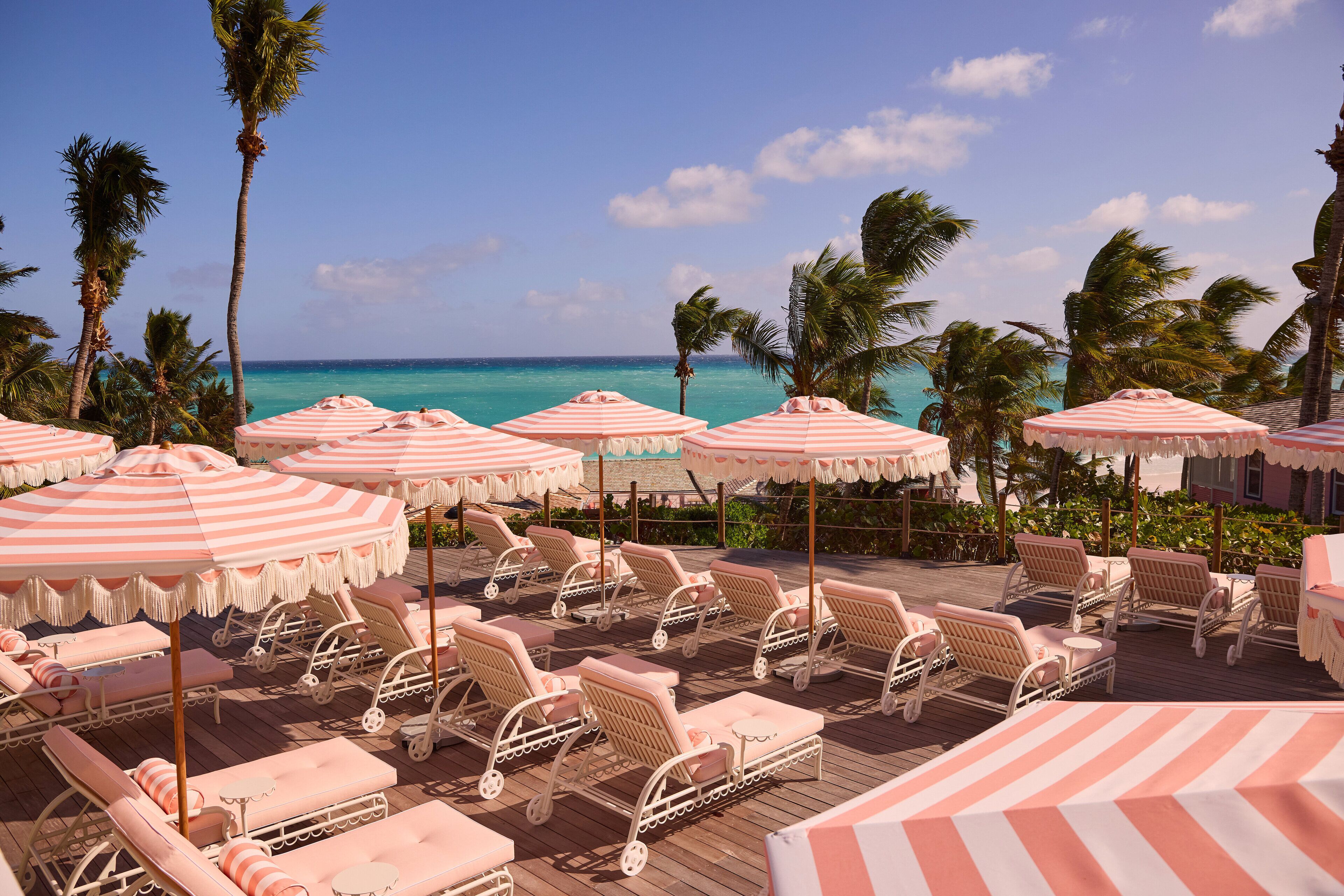 Ein Strandloungebereich mit gestreiften Sonnenschirmen und Korbmöbel-Loungesesseln mit Blick aufs Meer.