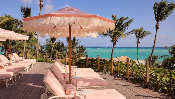 Une terrasse en bois avec des chaises longues roses et un grand parasol rayé.