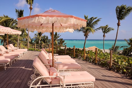 A wooden deck with pink lounge chairs and a large striped umbrella.