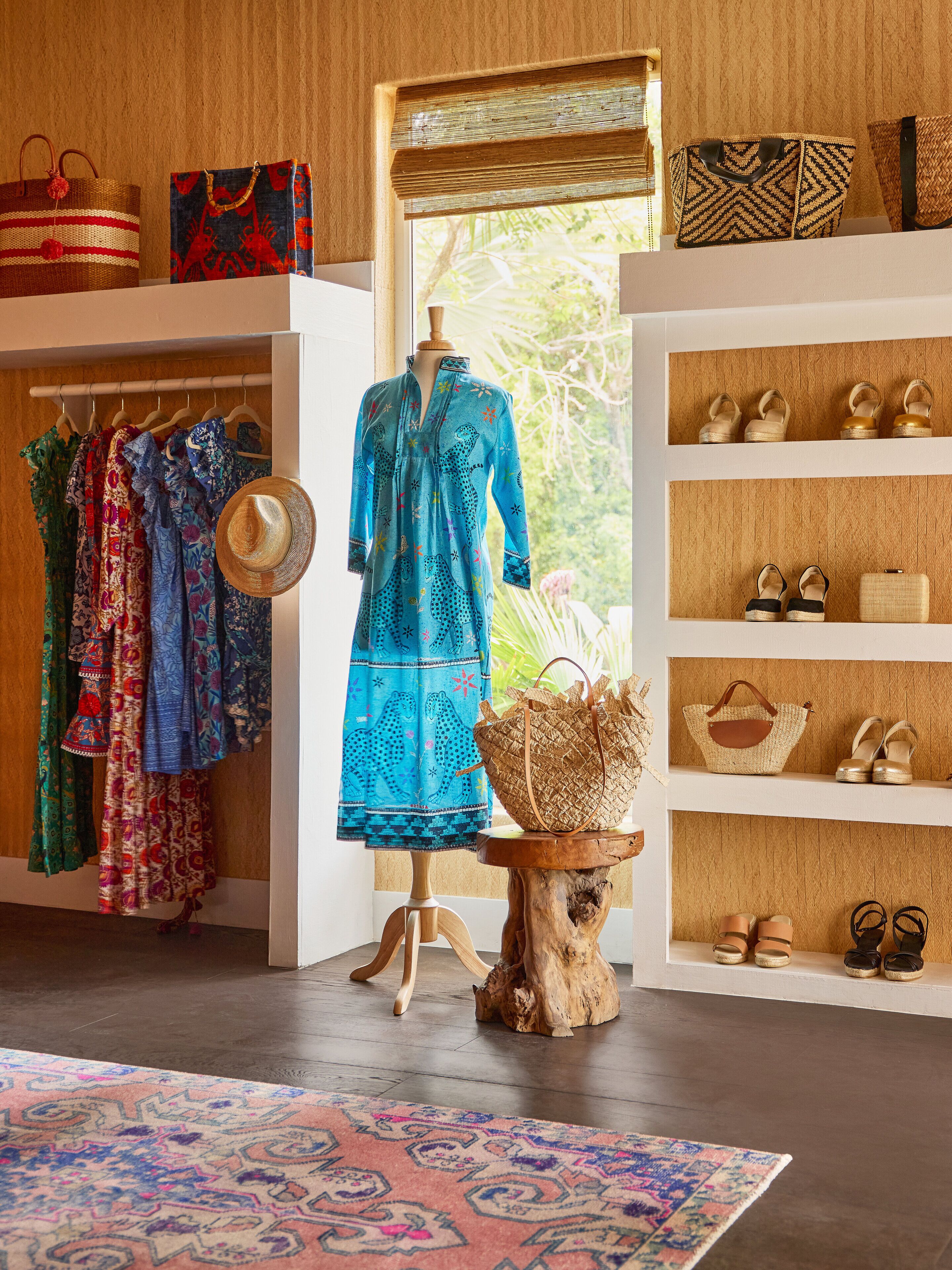 A boutique with a wooden interior, featuring a mannequin in a blue dress, shelves with shoes and handbags, and a patterned rug on the floor.