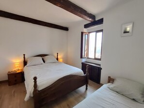 A bedroom with a wooden bed, bedside lamps, a window with a view, and a small bedside table.