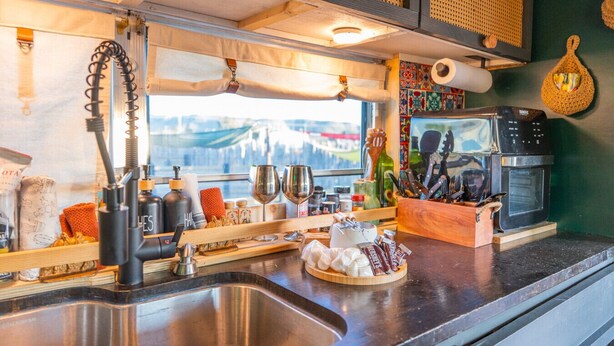 Una cocina con un lavamanos de acero inoxidable, una cafetera y un ventanal con vistas a un paisaje urbano.