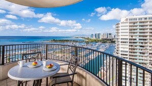 A balcony with a table and chairs, overlooking a marina with boats and a beach. - Hilton's Lagoon Tower 1-Bd Plus Ocean View: A Paradise with Endless Fun (Honolulu)