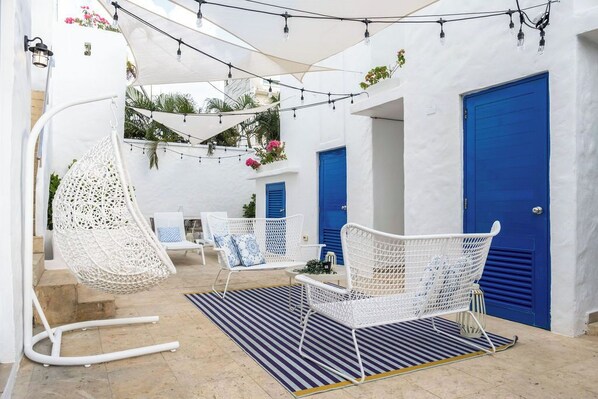 Une cour avec des meubles en osier peints en blanc, des portes bleues et des guirlandes lumineuses.