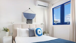Una habitación de hotel con una cama, un adorno de macramé en la pared, aire acondicionado, una ventana con cortinas y una mesita de noche con lámpara.