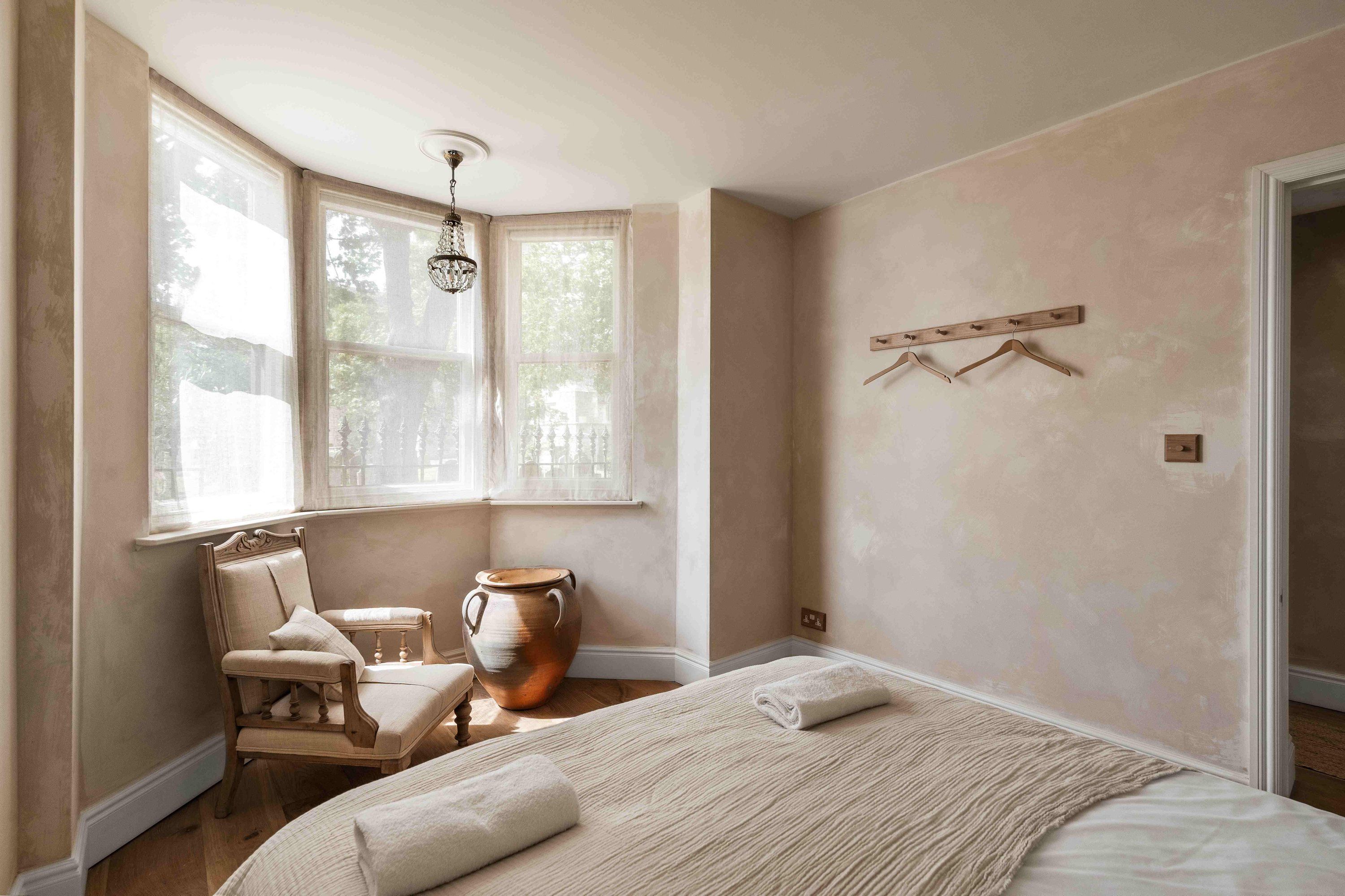 A bedroom with a large bed, a chair, a table, and a vase.