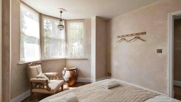 A bedroom with a large bed, a chair, a table, and a vase.