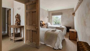Une chambre avec deux lits, une porte en bois, une petite table avec un bol et un radiateur.