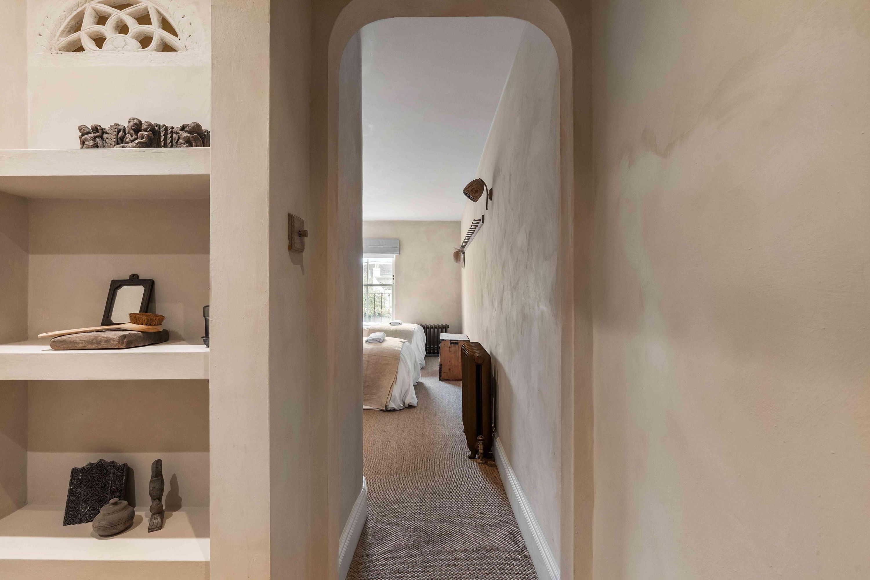 A narrow hallway leading to a bedroom with a radiator and a bed.