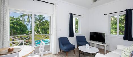 Ein Zimmer mit Blick auf einen Pool, weiße Möbel, ein Fernseher und ein Deckenventilator.