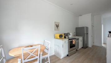 Een kleine keuken met witte kastjes, een houten eettafel en stoelen.