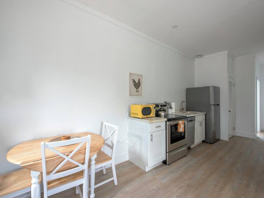 Een kleine keuken met witte kastjes, een houten eettafel en stoelen.