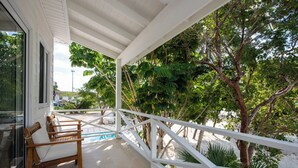 A covered outdoor area with a pool, wooden chairs, and a white railing. - Laughing Bird Suites (Governor's Harbour)