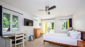 A bedroom with a bed, a desk, a chair, a TV, and a ceiling fan. - Laughing Bird Suites (Governor's Harbour)