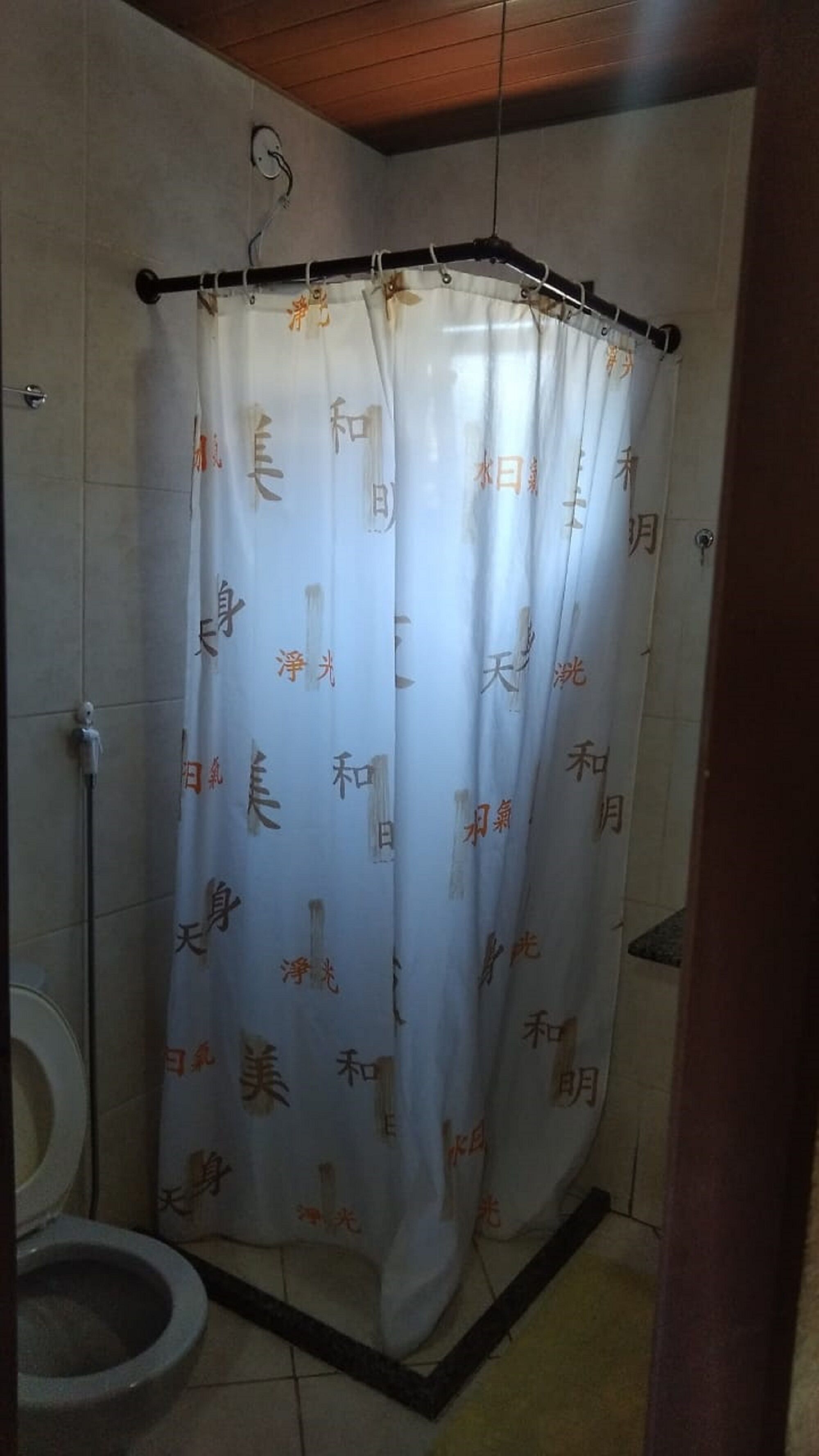 Une salle de bain avec un rideau de douche orné de caractères chinois, des toilettes et un plafond en bois.