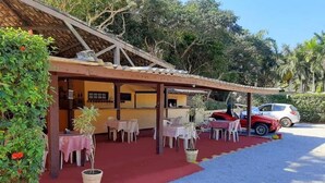 A covered outdoor seating area with tables and chairs, a vehicle parked nearby, and a building with a tiled roof. - A Casa do Pablo (Buzios)