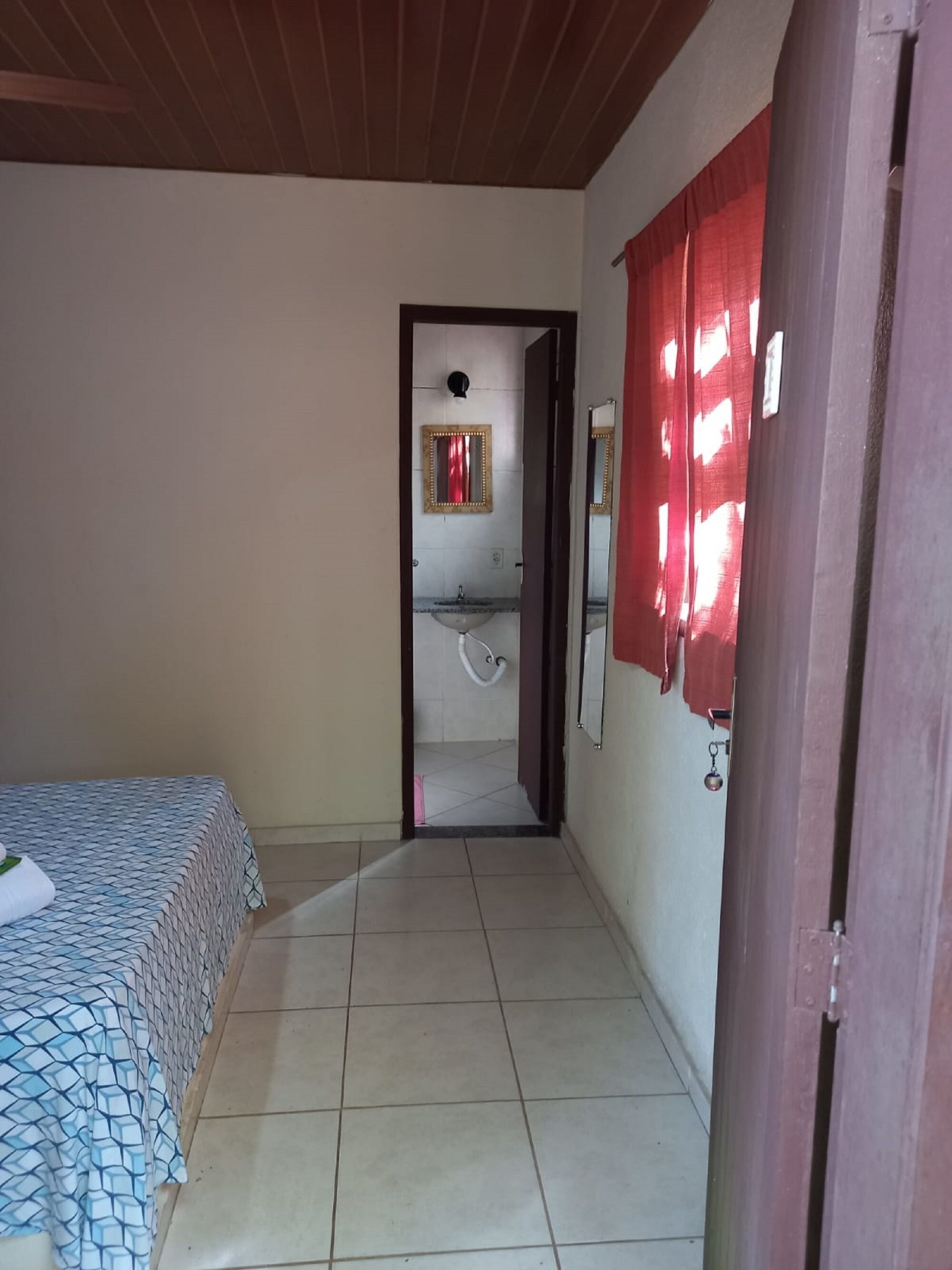A narrow hallway leading to a bathroom with a sink and mirror. A bed with a patterned bedspread is visible on the left.