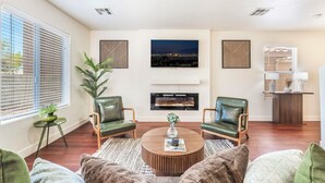 A modern living room with two green leather armchairs, a round coffee table, and a flat-screen TV mounted above a fireplace. - Near Strip & Airport - 3BR + Golf (Las Vegas)