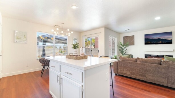 A modern kitchen with white cabinetry, a central island, and a dining area with a chair. - Near Strip & Airport - 3BR + Golf (Las Vegas)