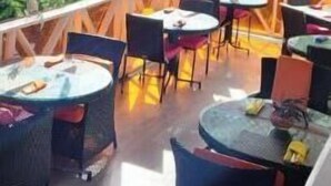 Un espace extérieur aménagé en terrasse, avec des tables et des chaises rondes, un ventilateur de plafond et une vue sur la verdure.