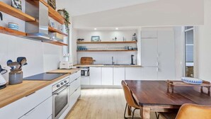 Una cocina moderna con armarios blancos, estantes de madera, una mesa de comedor y un horno empotrado.