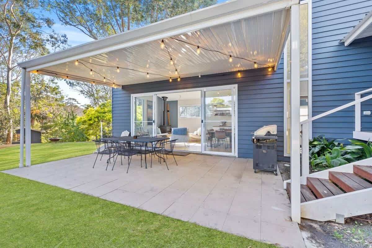 A covered patio with a table and chairs, a grill, and a sliding glass door leading to an interior space.