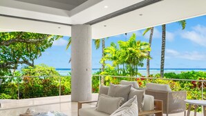 Una sala de estar moderna con un ventanal grande con vista a una playa tropical y al océano.